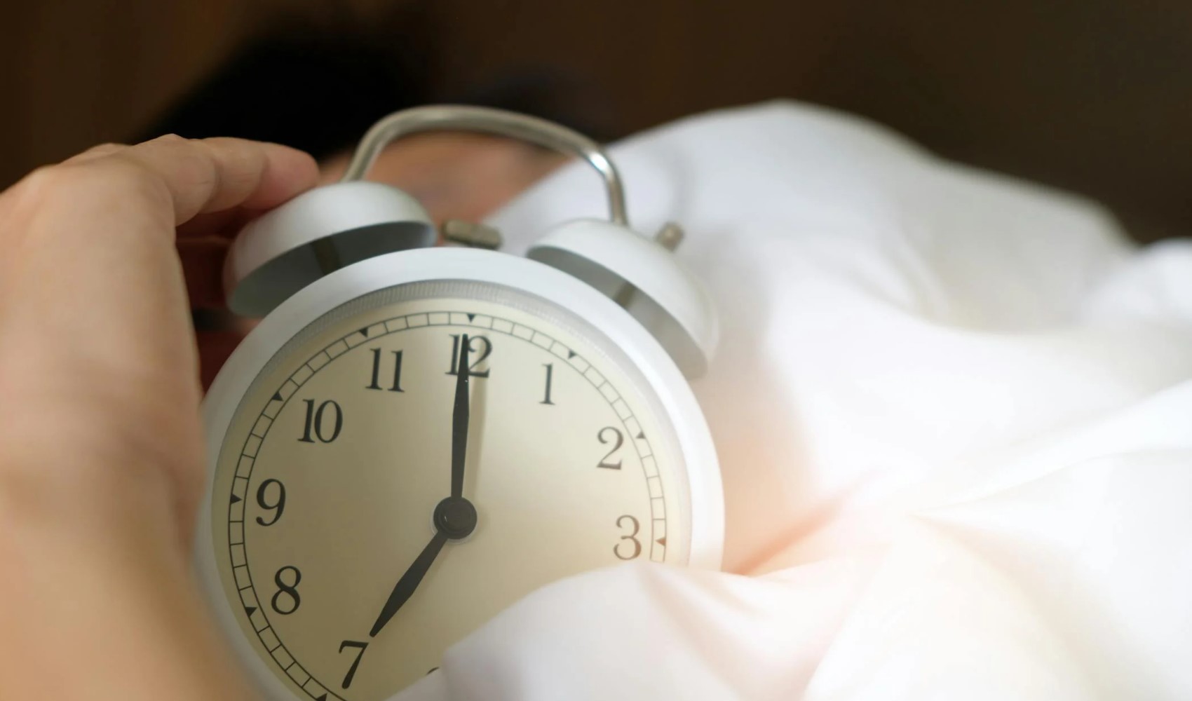 Yatakta alarm saatinin yanında uyumaya çalışan bir kişi.