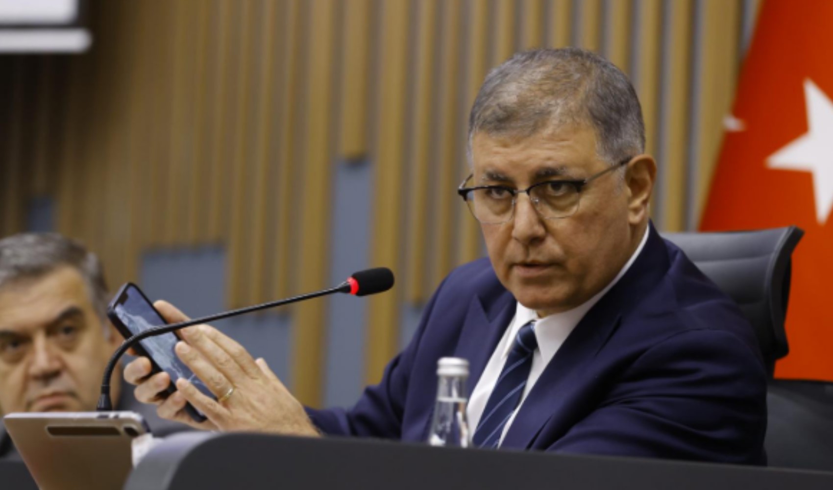 Cemil Tugay toplantı salonunda elinde telefonla konuşuyor.