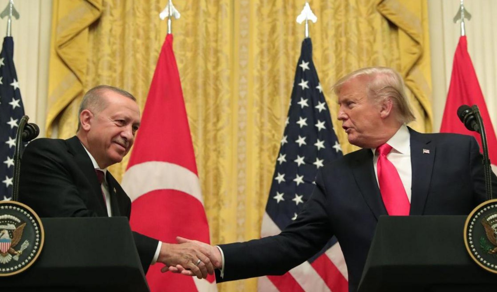 Recep Tayyip Erdoğan ve Donald Trump, Türkiye ve ABD bayrakları önünde tokalaşıyor.