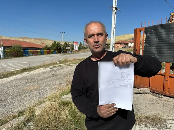 Murat Em stands in an open area holding a document.