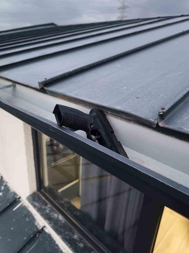 A black handgun is seen resting on the edge of a roof.