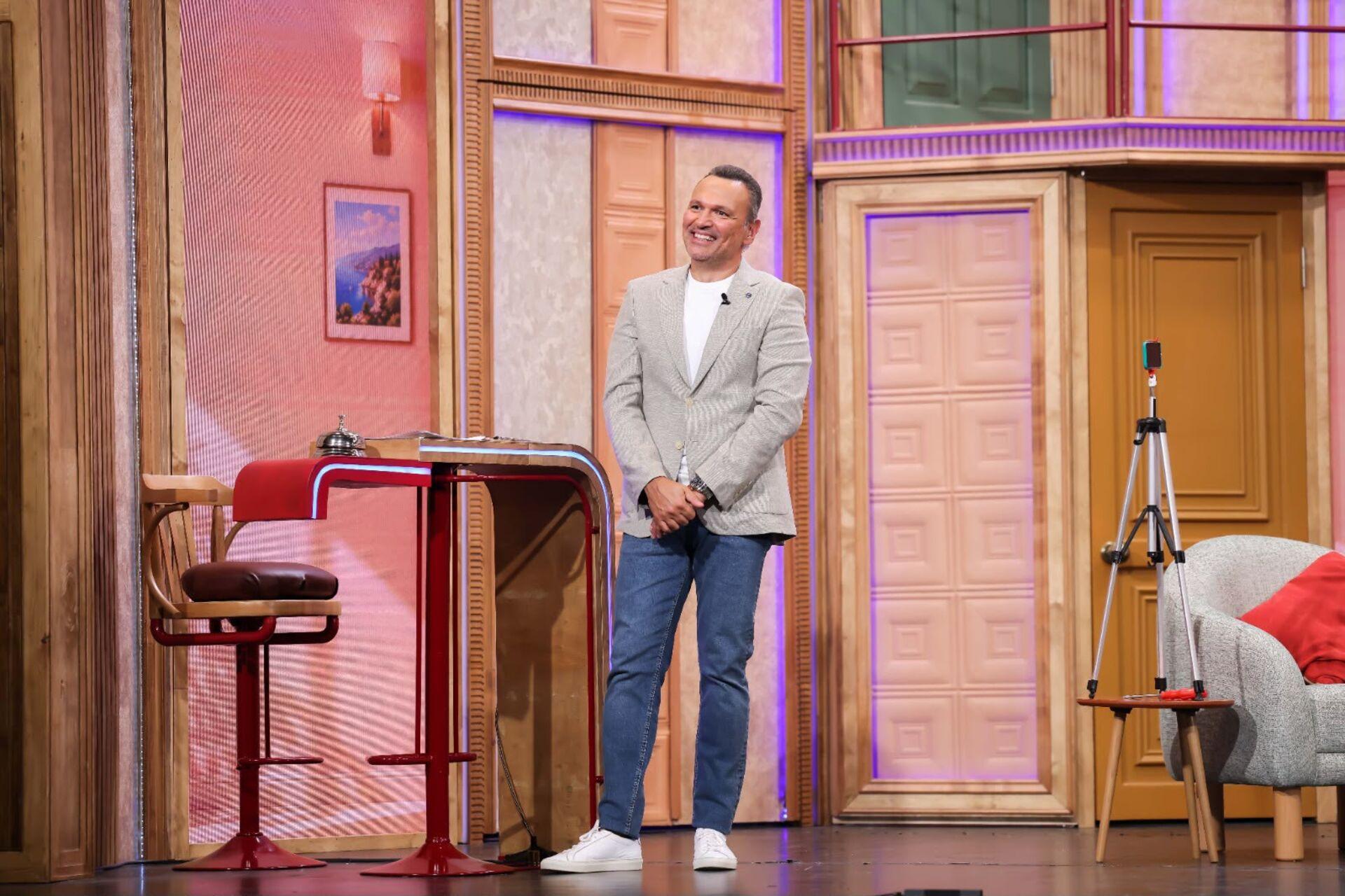 Mert Fırat, Güldür Güldür Show sahnesinde dekorlar arasında gülümserken görülüyor.