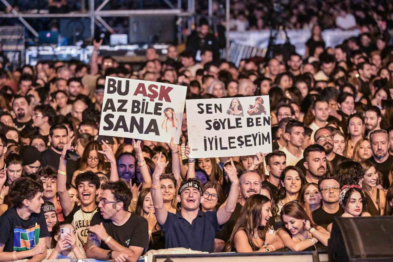 Kalabalık içinde 'Bu aşk az bile sana' ve 'Sen söyle ben iyileşeyim' yazılı pankartlar görülüyor.