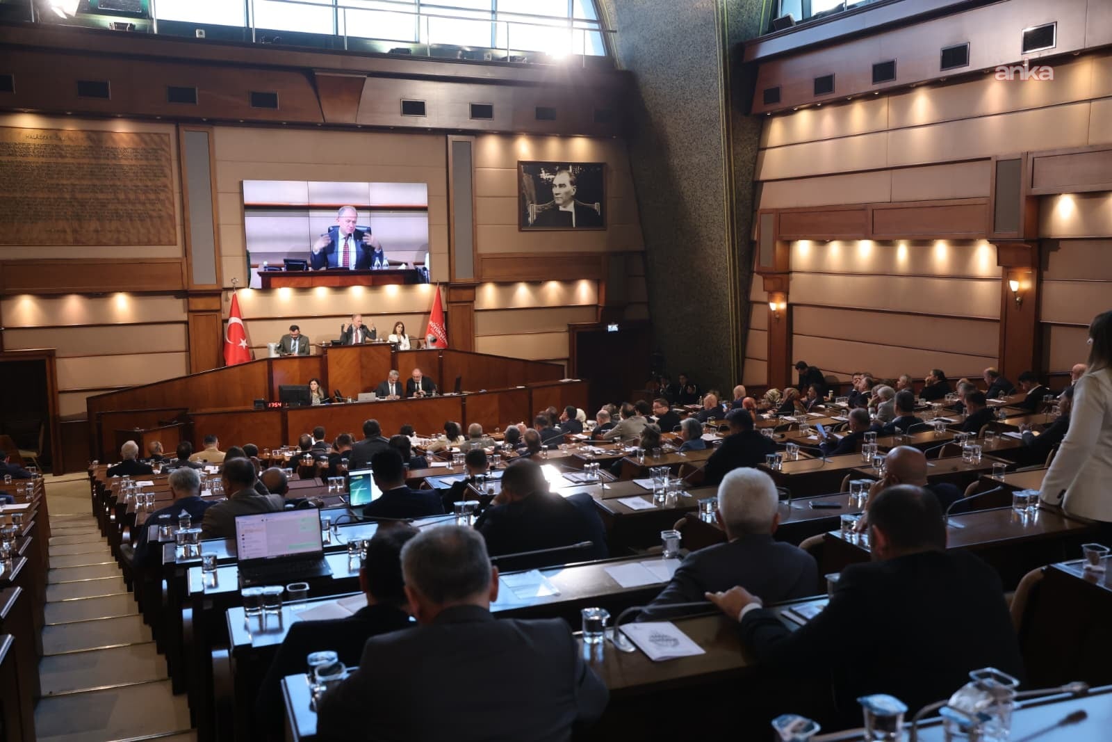 Vista grandangolare della sala dell'Assemblea dell'IMM, i membri che seguono la seduta e lo schermo del discorso.