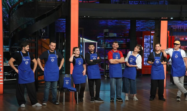 MasterChef stüdyosunda mavi önlüklü yarışmacılar yan yana duruyor.