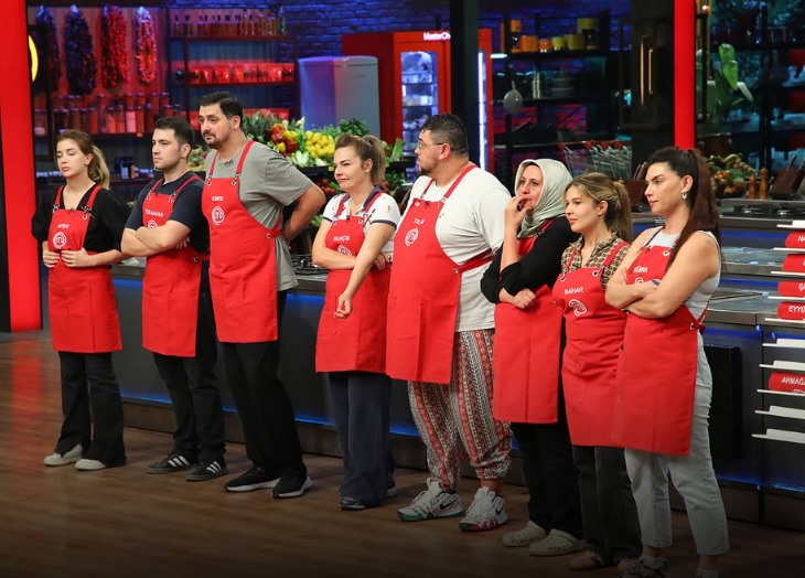 MasterChef stüdyosunda kırmızı önlüklü yarışmacılar yan yana duruyor.