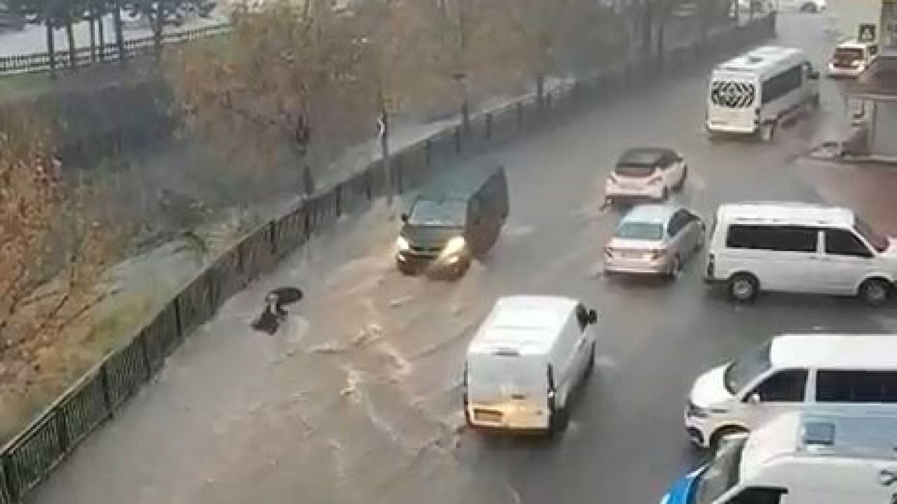 Yağış altında araçların ilerlediği, yol kenarında su birikintilerinin oluştuğu bir cadde.