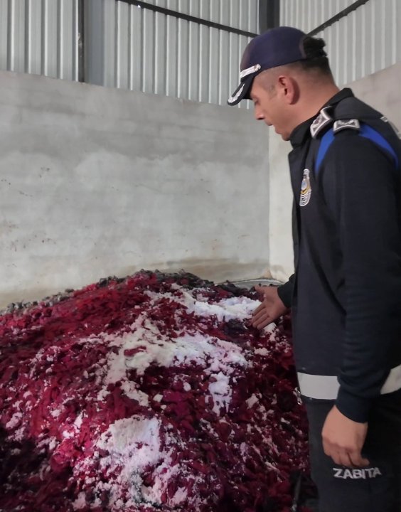 A municipal police officer examining red-colored food products left in the open in the warehouse.