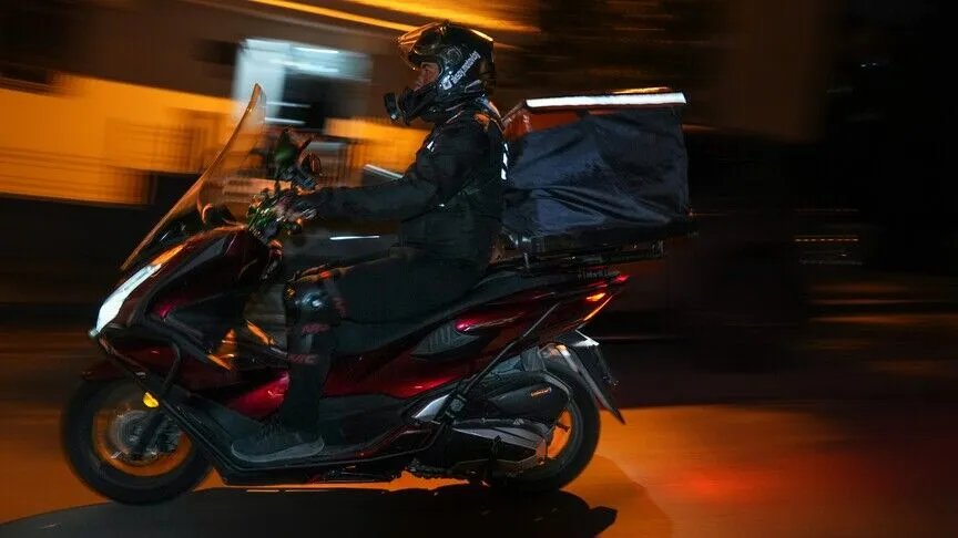 A motorcycle courier driving in traffic at night.