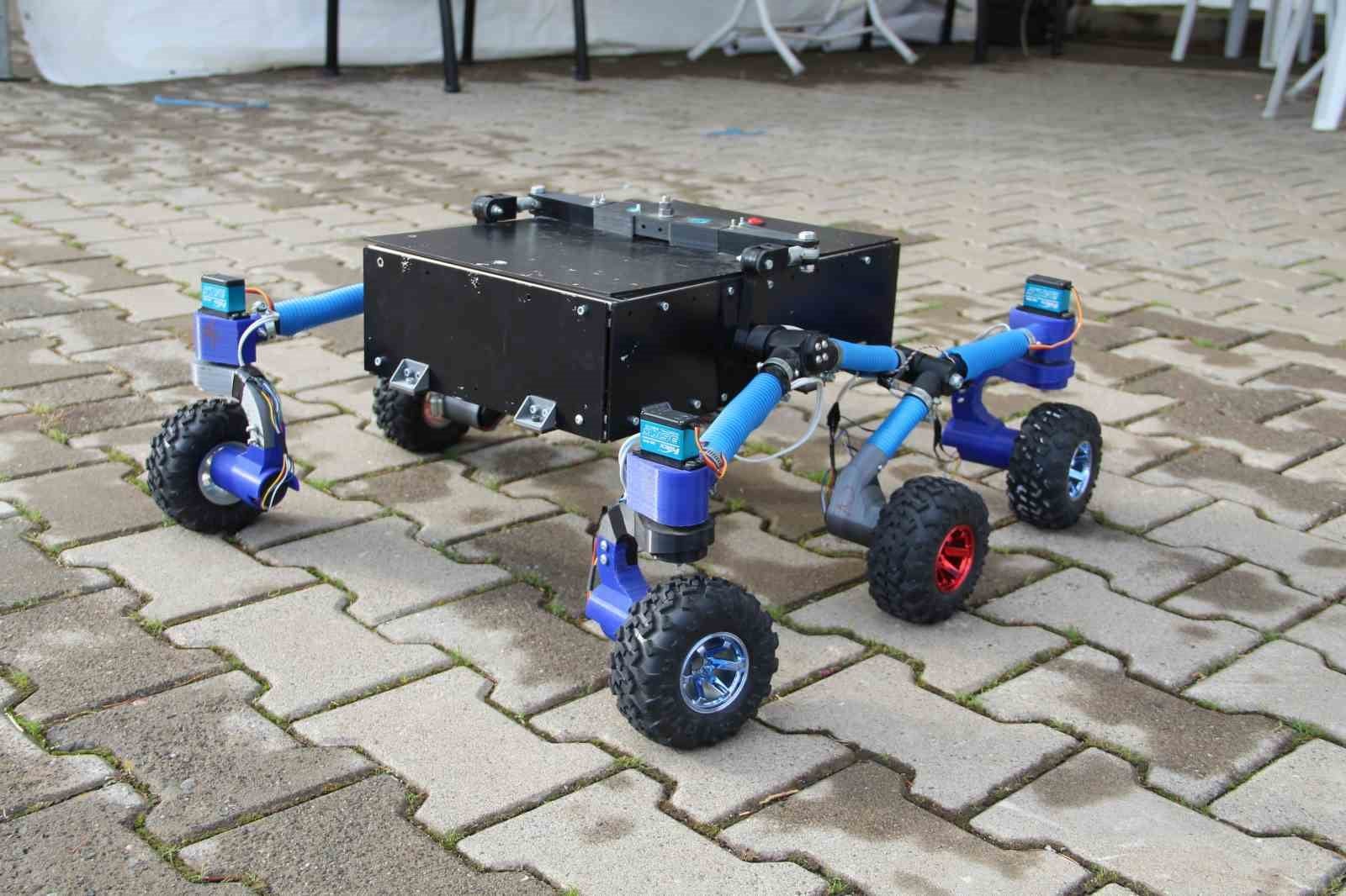 Altı tekerlekli, siyah gövdeli arama kurtarma robotu prototipi taş zemin üzerinde görülüyor.