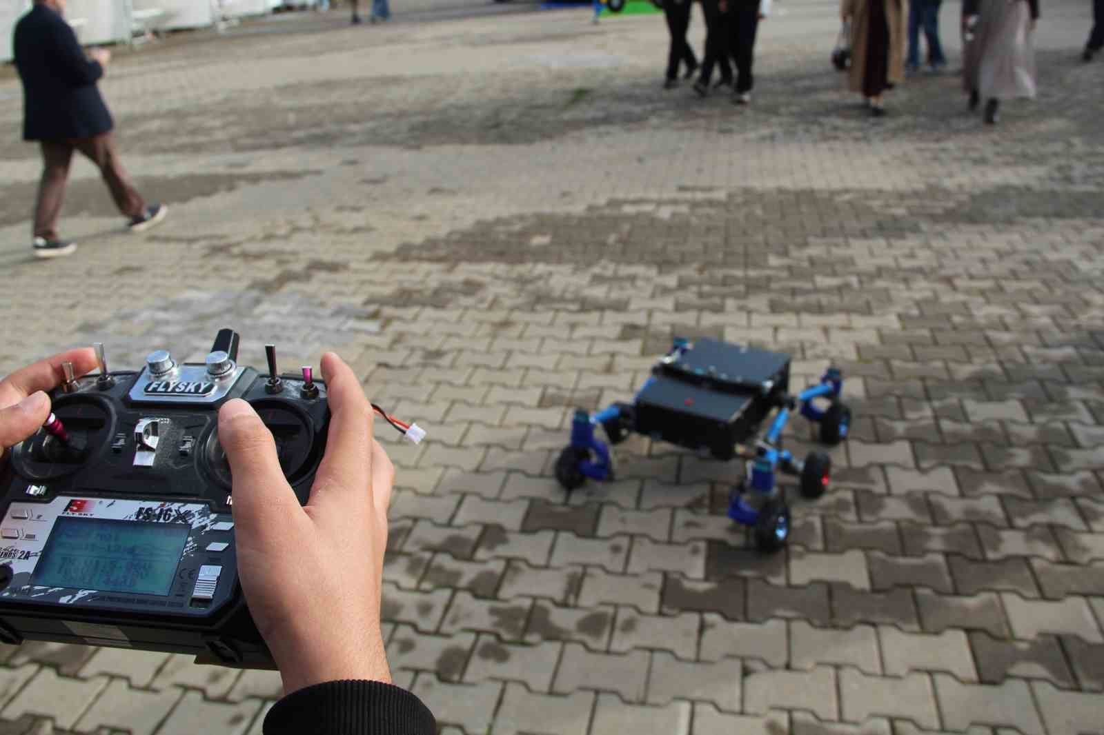 Yakından görülen bir uzaktan kumanda ile arka planda hareket eden robot yer alıyor.