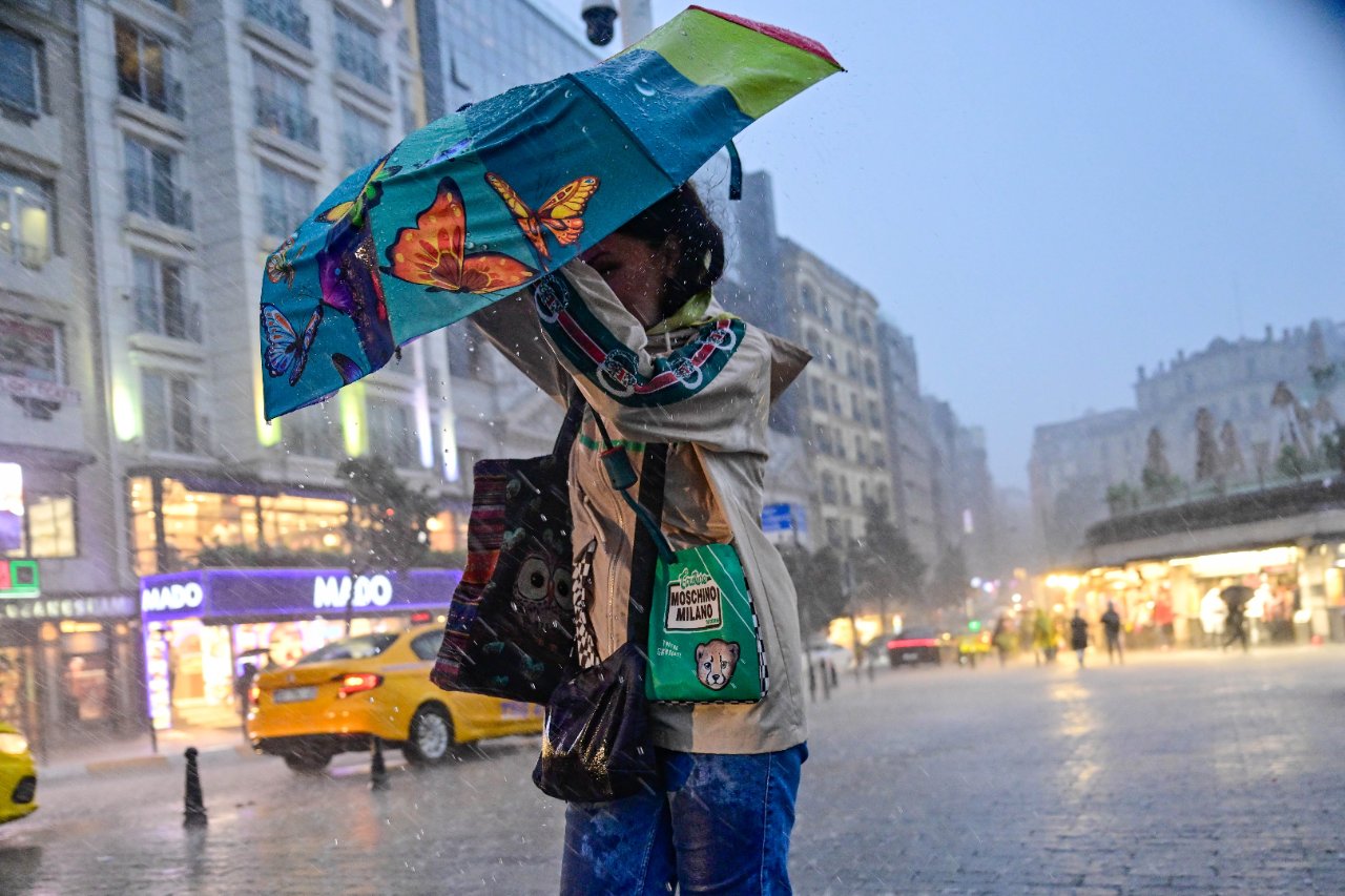 Sağanak altında şemsiye kullanan bir kişi ve ıslak kent meydanı.
