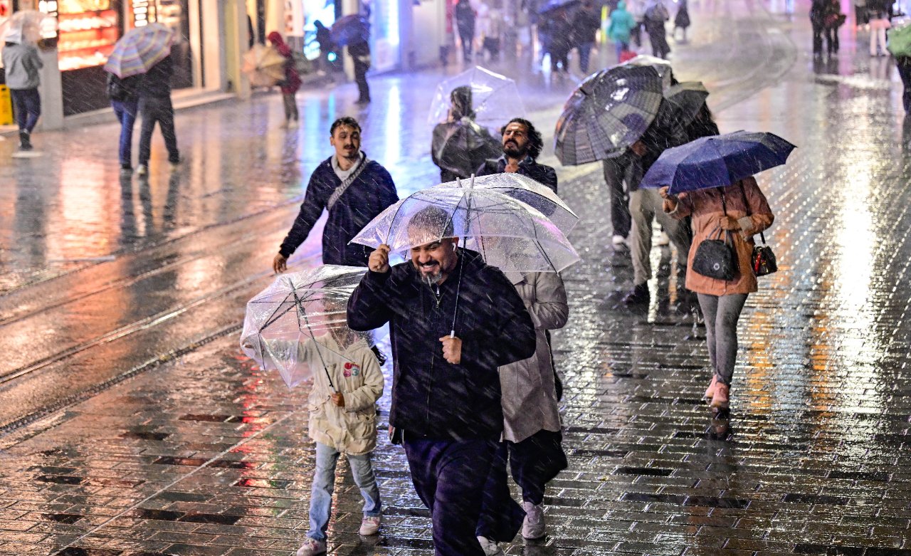 Yağmurlu bir caddede şemsiyelerle yürüyen insanlar görülüyor.