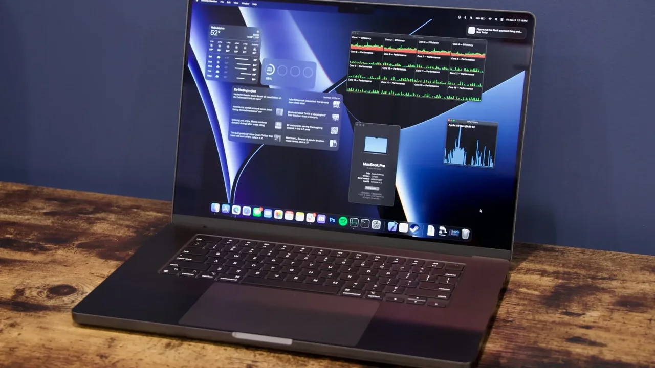 Ahşap masa üzerinde açık duran MacBook Pro ekranında performans göstergeleri ve sistem pencereleri görülüyor.
