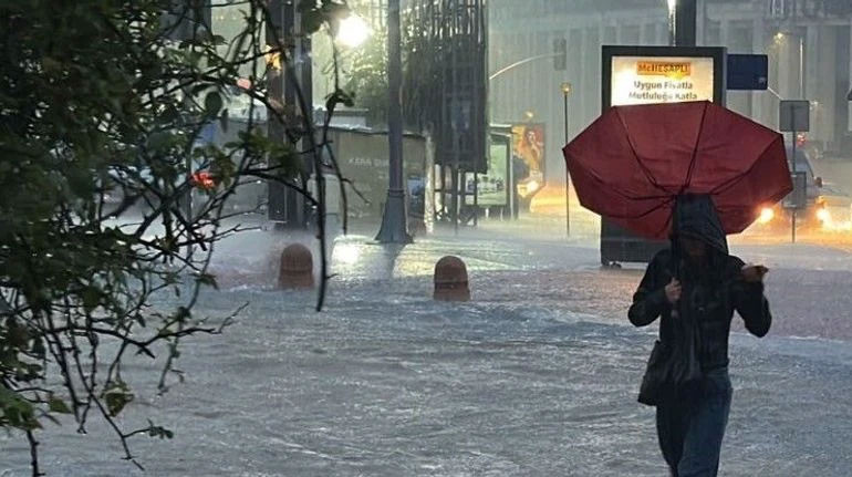 Şiddetli yağış altında suyla kaplanan caddede şemsiyeli yaya.