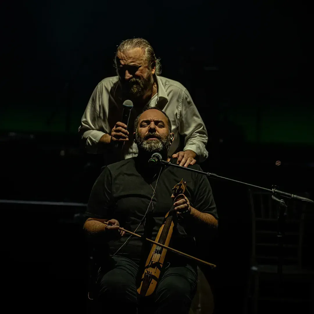Sahnede Volkan Konak'ın, enstrüman çalan Selim Bölükbaşı'nın arkasında mikrofonla görüldüğü konser fotoğrafı.