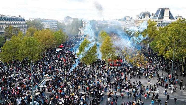A crowded protest demonstration in Paris and smoke rising in the streets.