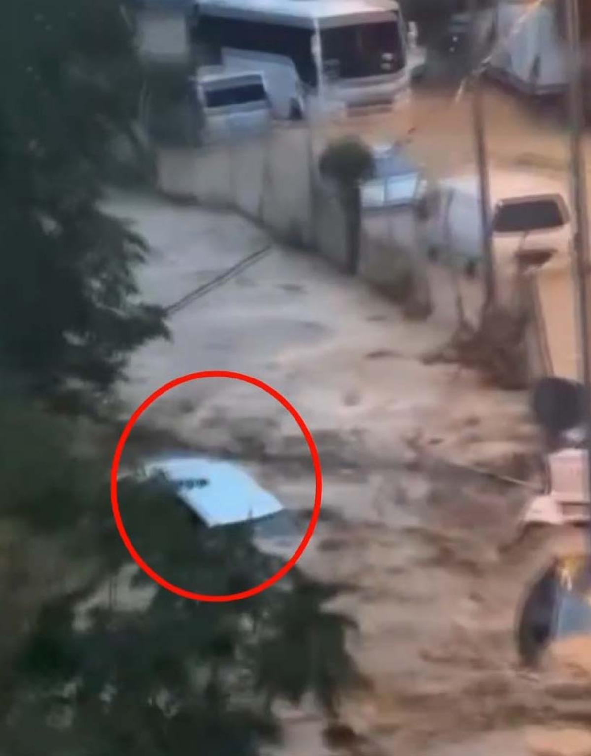 Sokakta hızla akan çamurlu sel suyunda sürüklenen bir aracın kırmızı daireyle işaretlendiği görüntü.