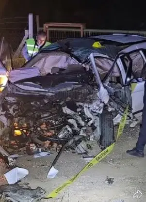 The heavily damaged vehicle and the crime scene tape at the site of the traffic accident that occurred at night.