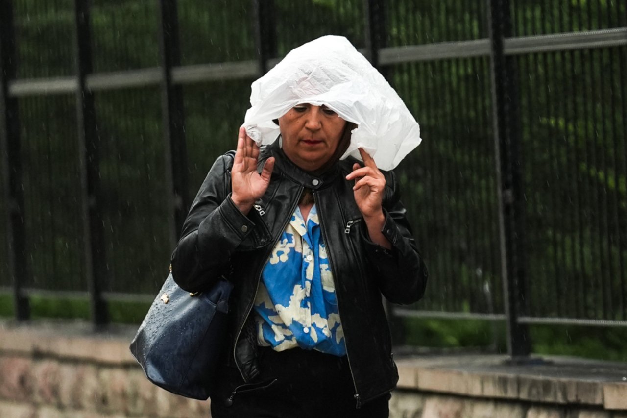 Yağmur altında başını plastik örtüyle koruyan bir kişi.
