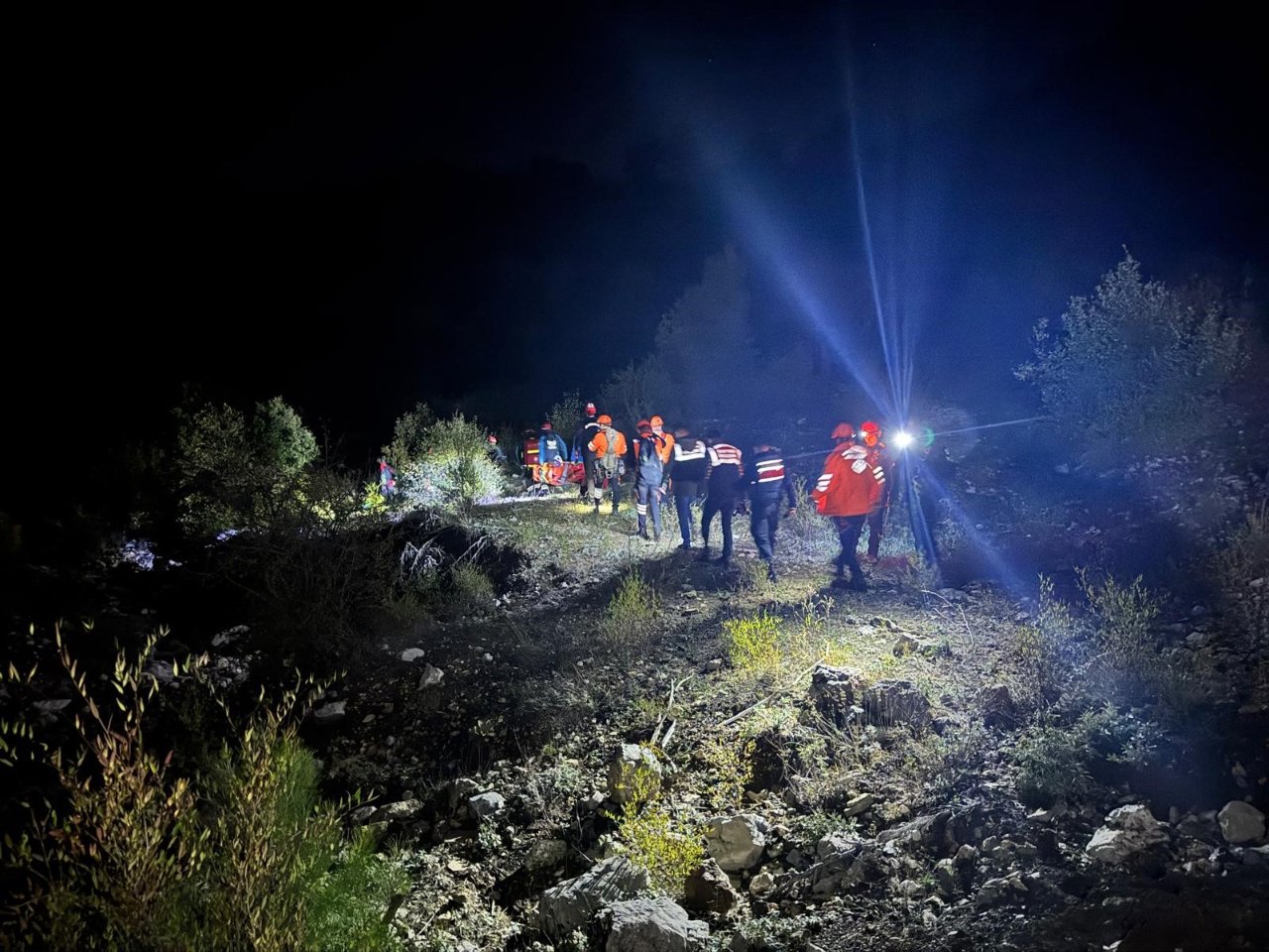 Équipes de recherche et de sauvetage progressant sur un terrain escarpé dans l'obscurité de la nuit avec des lampes et des projecteurs.