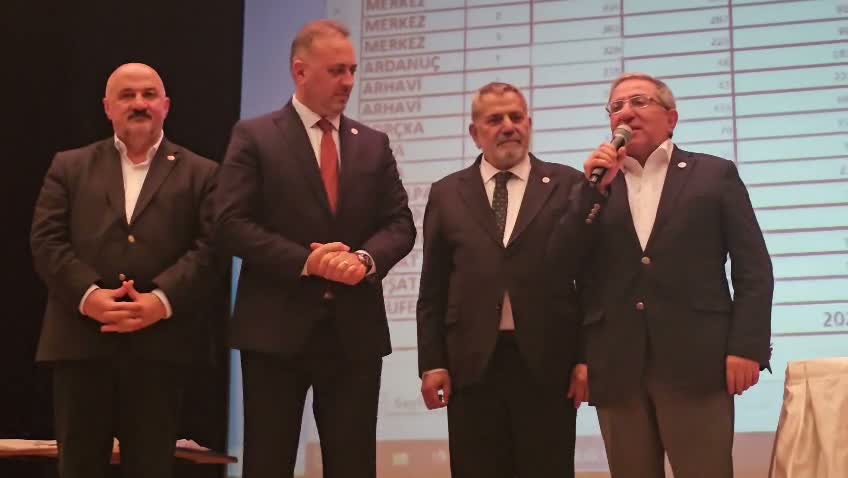 Sahnede mikrofonla konuşan parti temsilcileri ve sonuçların yer aldığı ekran.