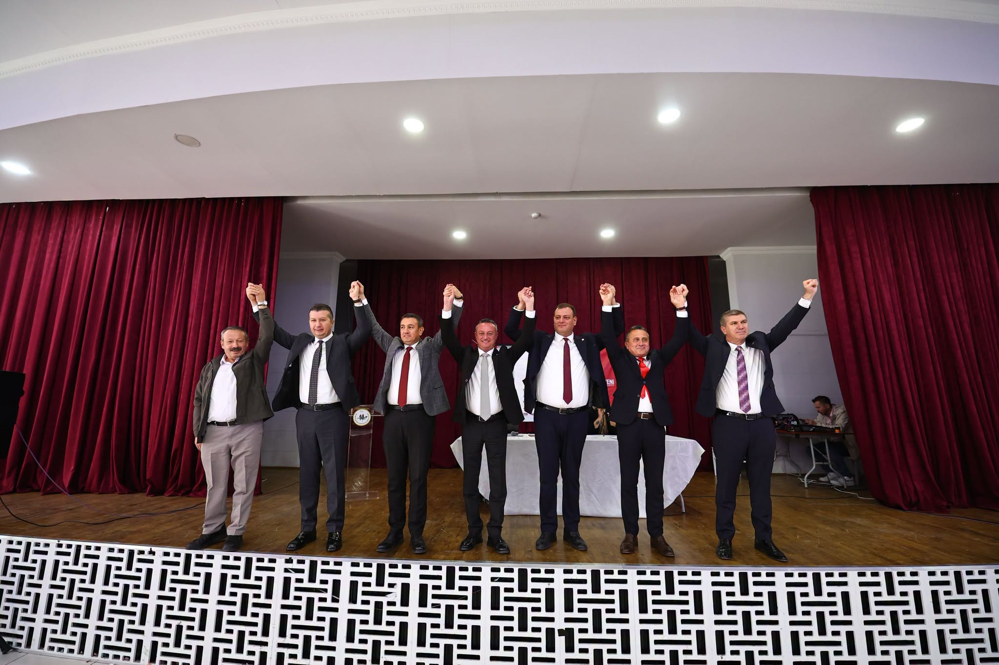 Sahnede ellerini kaldıran partililer ve kırmızı perde önünde düzenlenen toplantı.