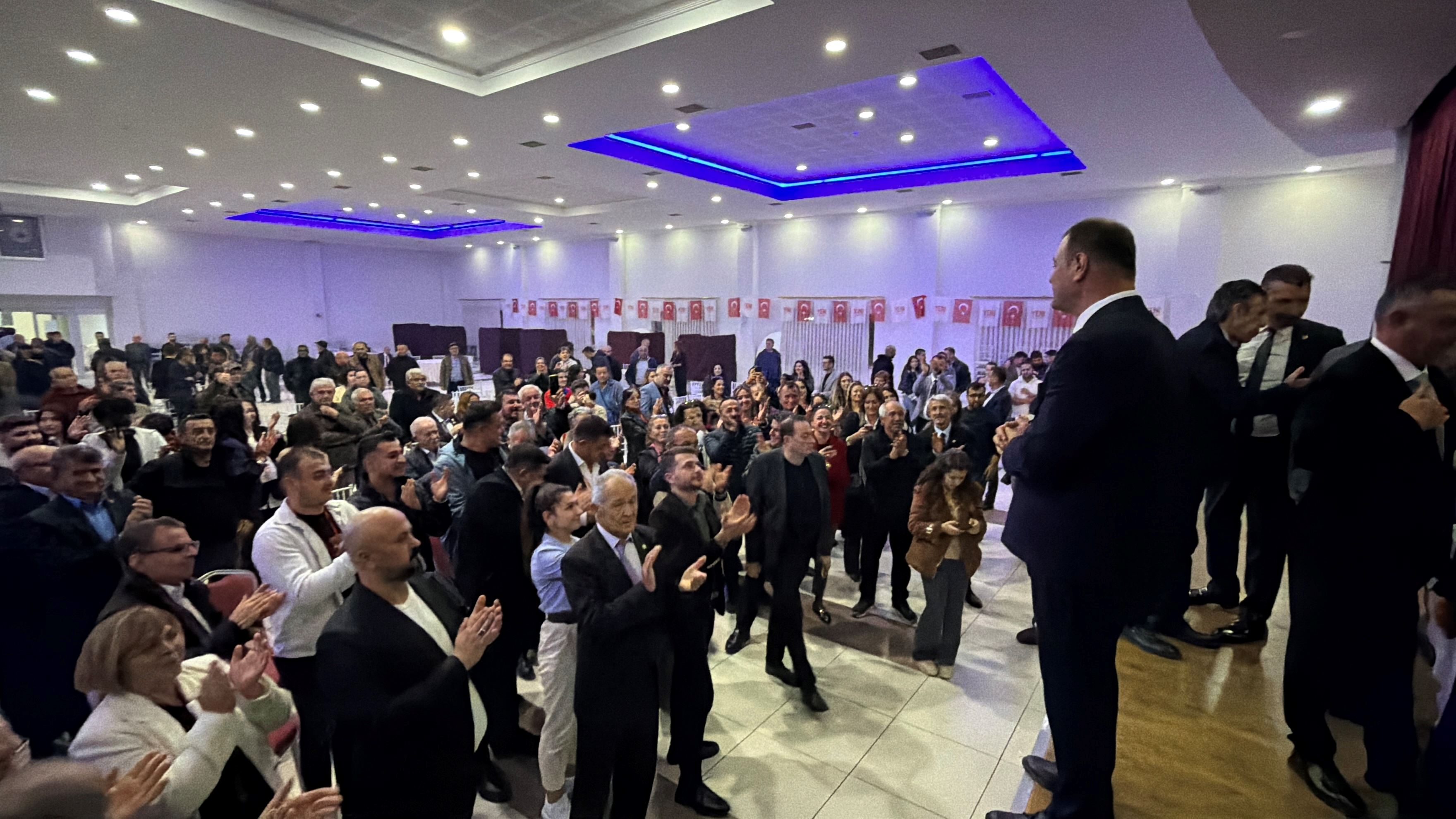 Kalabalık bir salonda oturan ve alkışlayan partililer görülüyor.