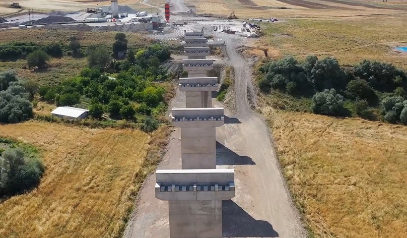 Concrete bridge piers lined up in rural terrain, service roads, and the construction site area.