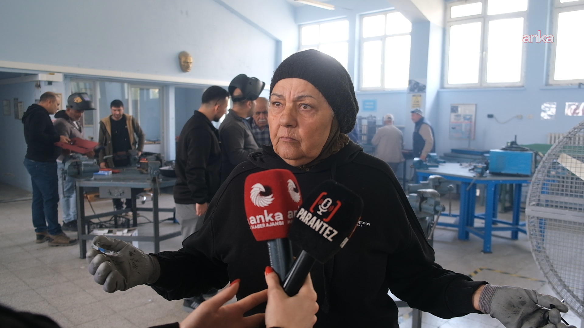 Rahime Öztunç, atölyede mikrofonlara konuşurken arka planda kursiyerler çalışıyor.