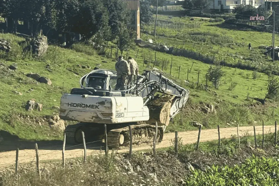 Kırsal alanda yol kenarında duran beyaz iş makinesi ve çevrede evler.