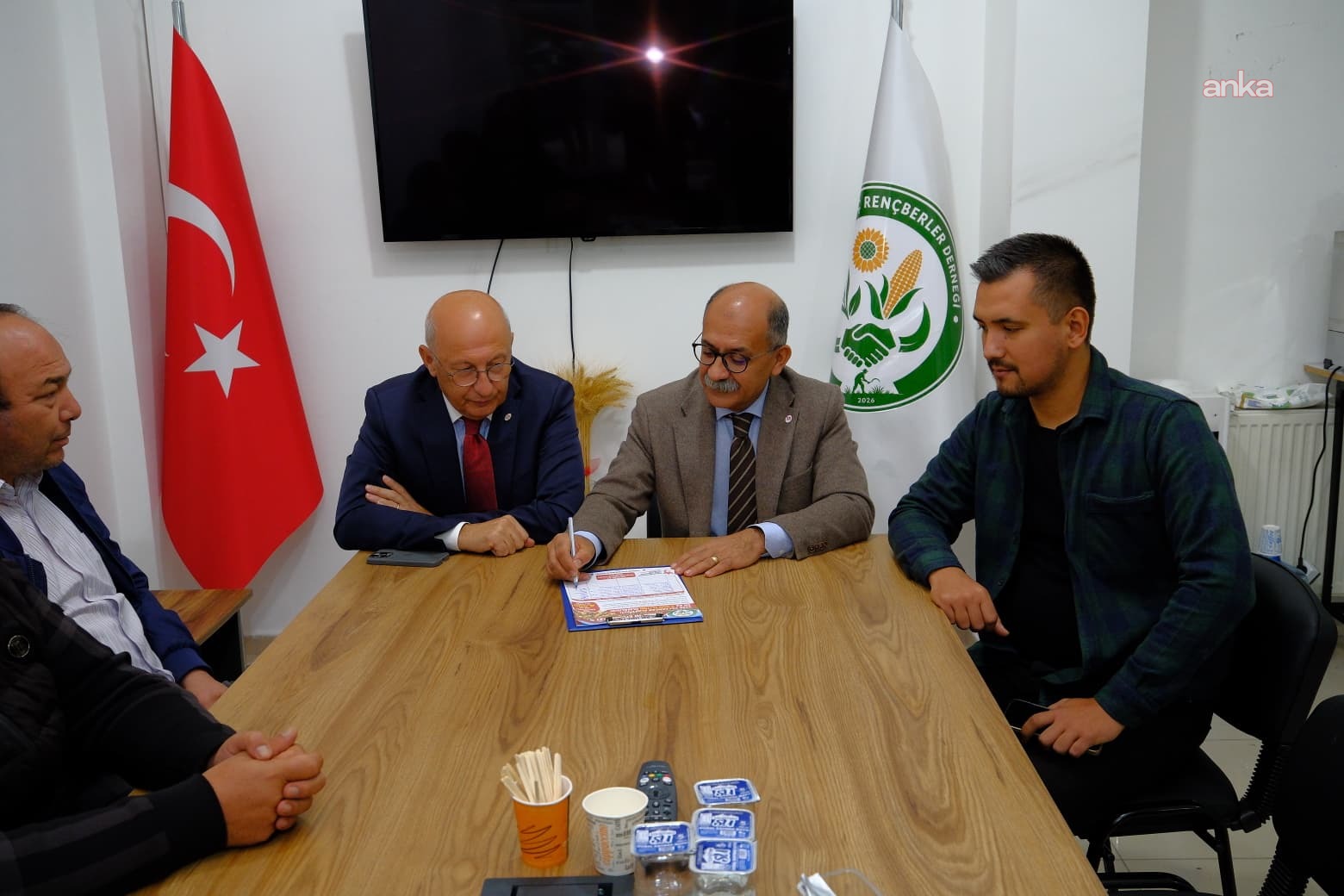 Dernek odasında bir siyasetçinin imza formunu imzaladığı, yanında dernek temsilcilerinin bulunduğu görüntü.