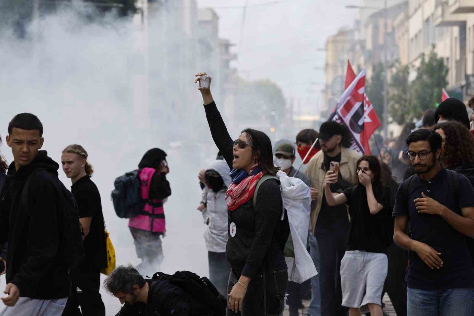 Dumanın yükseldiği bir caddede protestocular ve öğrenciler görülüyor.