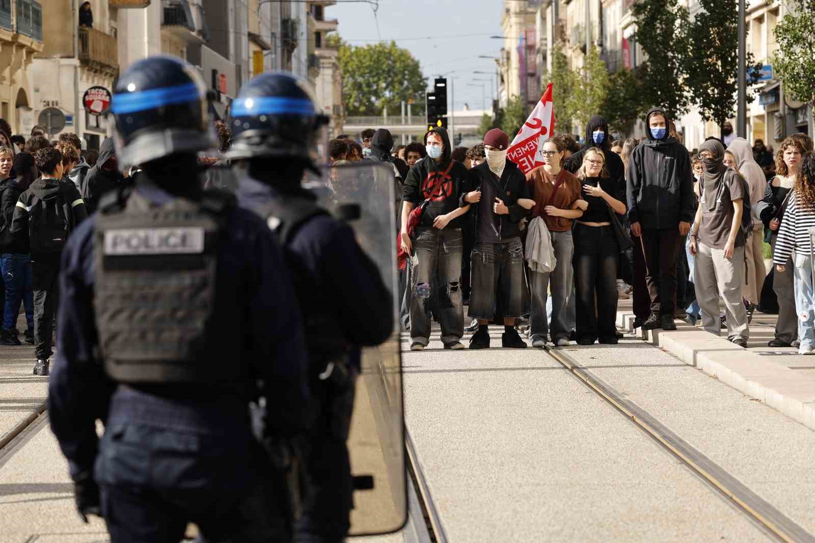 Bir caddede polislerin karşısında toplanmış kalabalık bir öğrenci grubu yer alıyor.