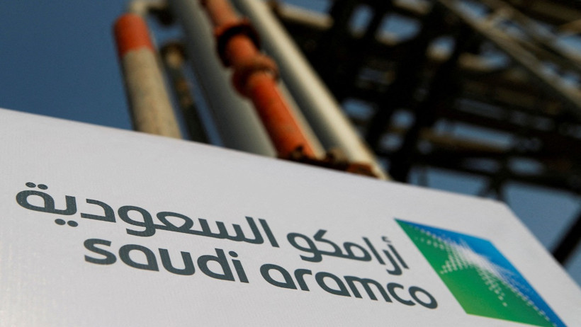 An energy facility sign reading Saudi Aramco with industrial pipelines in the background.