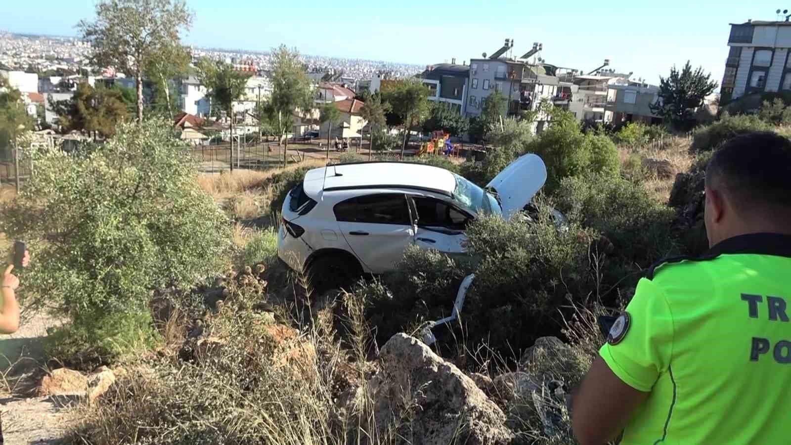 The accident site where the white car stopped in a rocky and bushy area, with a traffic police officer nearby.