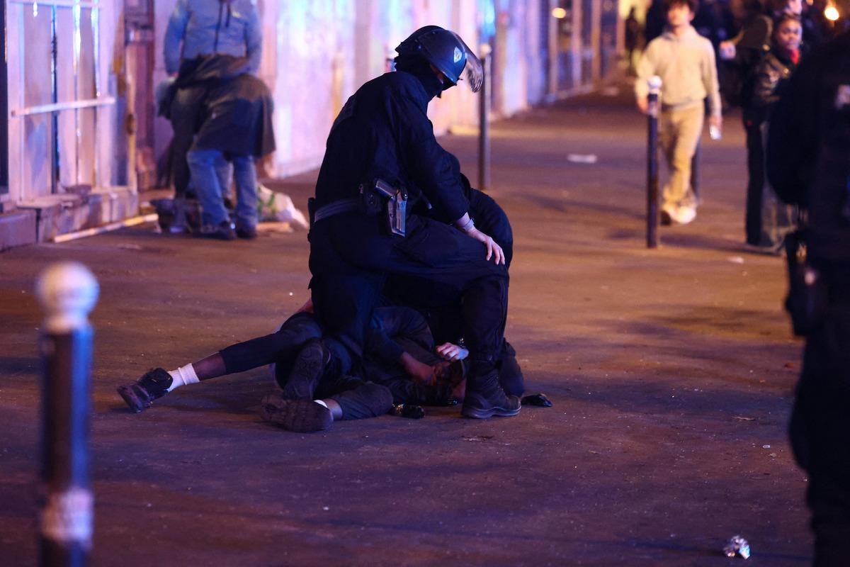 A protest scene where a police officer is intervening with people on the ground at night.