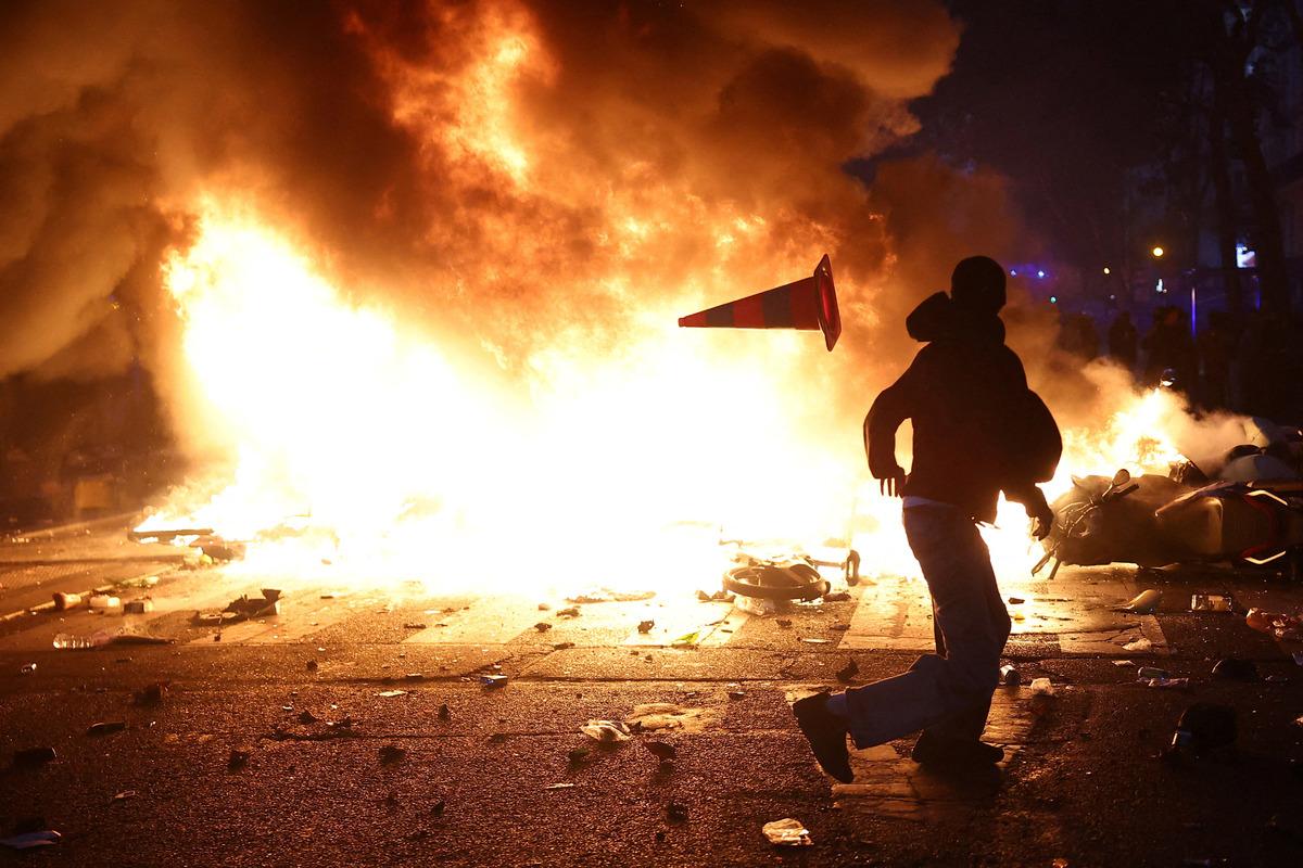 A protest image showing a person running in front of a large fire at night.