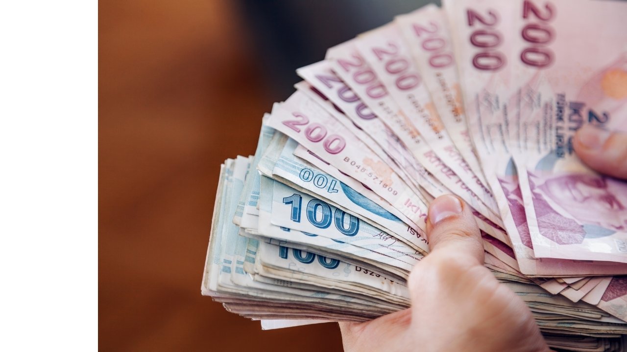 Close-up view of a large number of Turkish lira banknotes held in a hand.