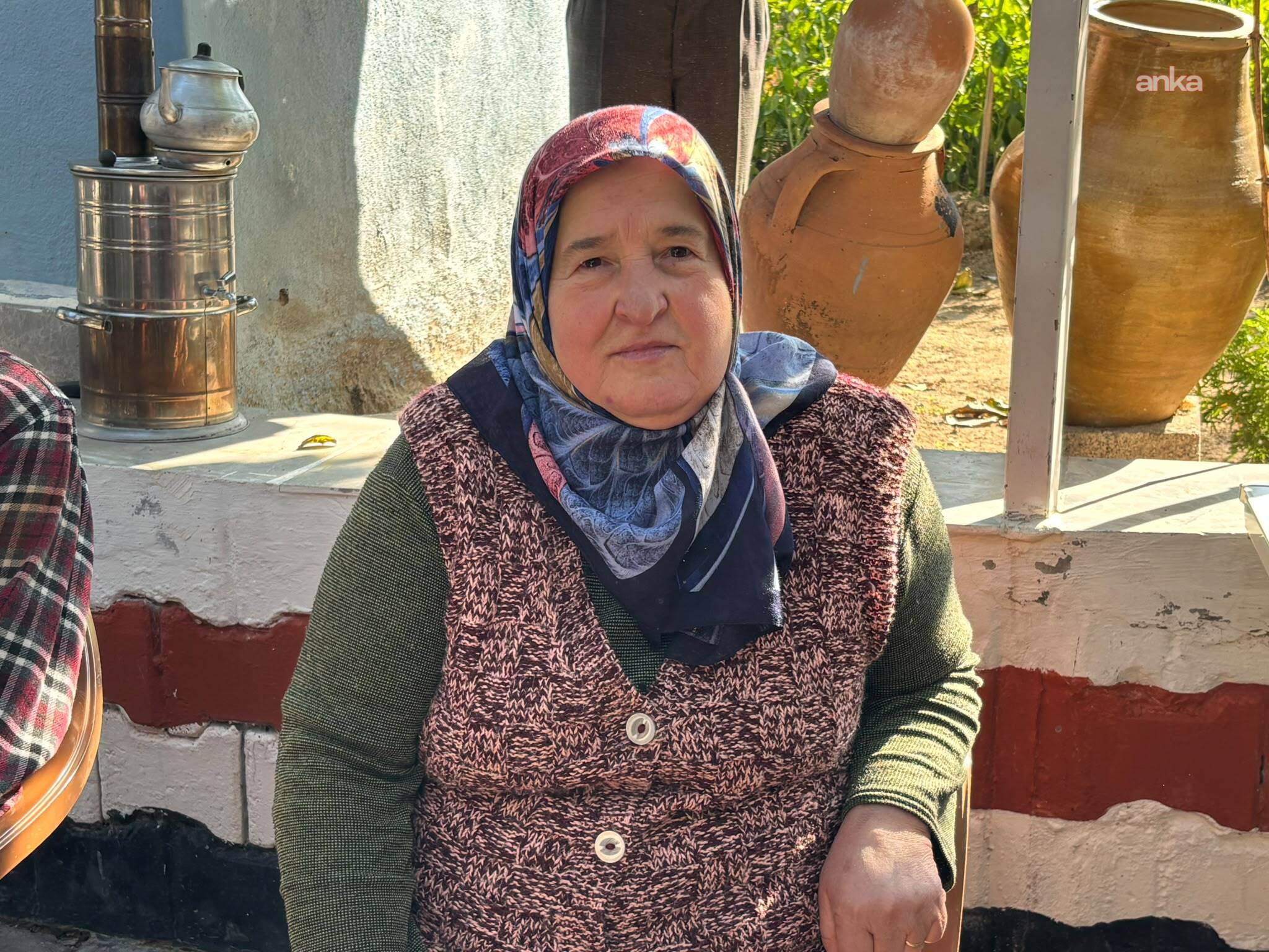 A woman wearing a headscarf looks at the camera in the courtyard of a rural house.