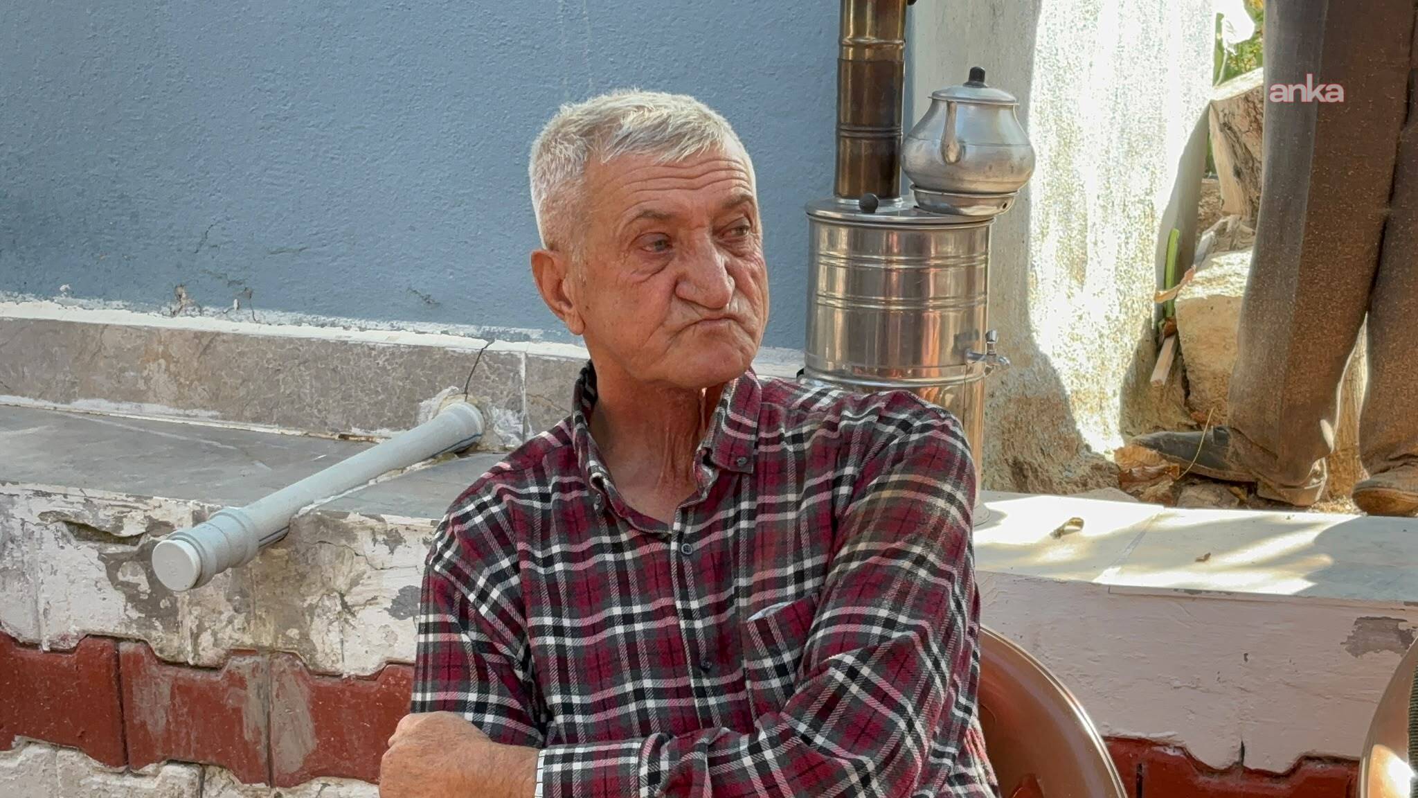 An elderly man is seen sitting in the courtyard of a rural house.