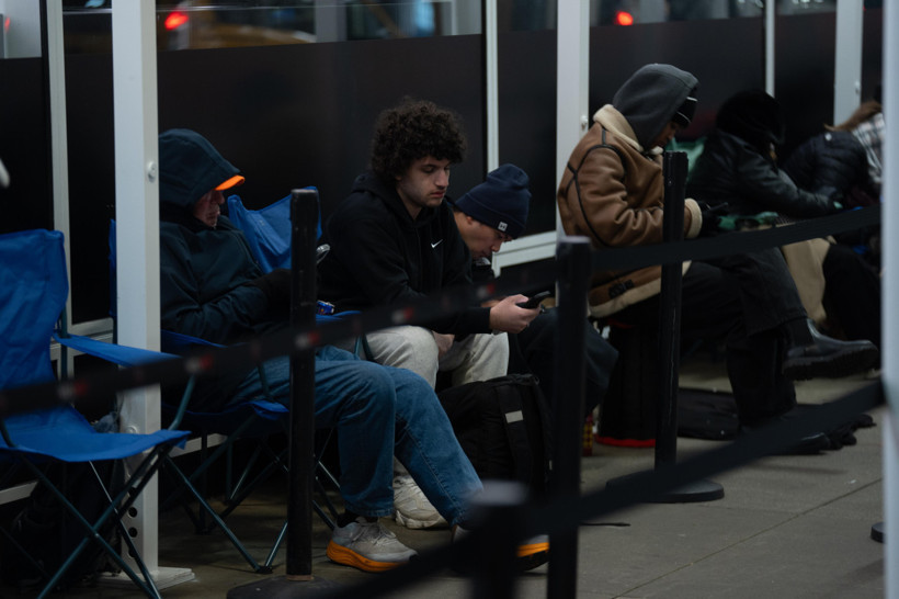 Bariyerler arasında sandalyelerde oturan ve telefon kullanan müşteriler.