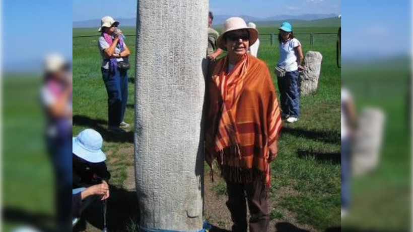 Prof. Dr. Gülçin Çandarlıoğlu’nun açık alanda, tarihi bir taş yazıtın yanında çekilmiş fotoğrafı.