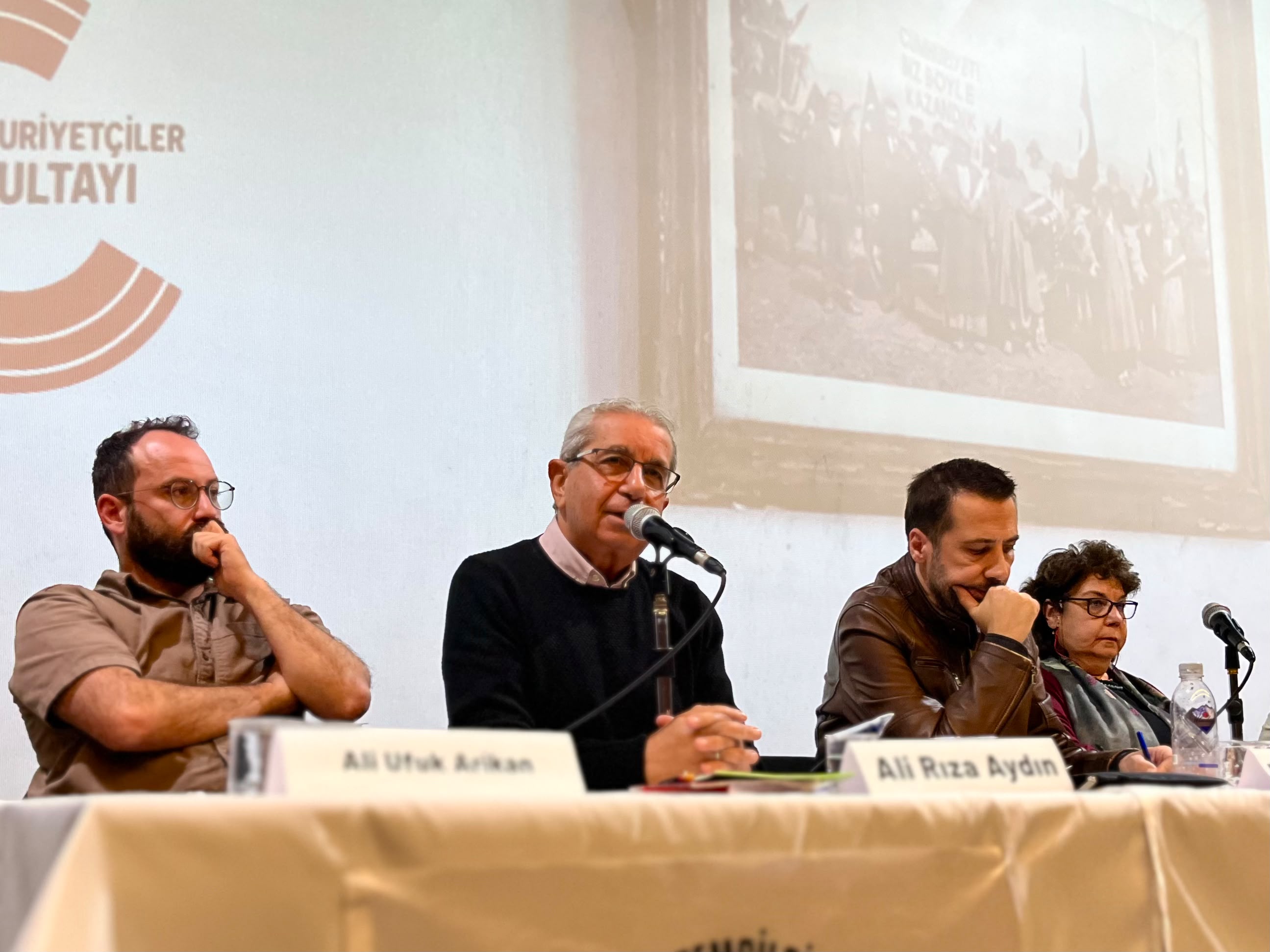 Ali Rıza Aydın’ın mikrofon başında konuştuğu panel görüntüsü.