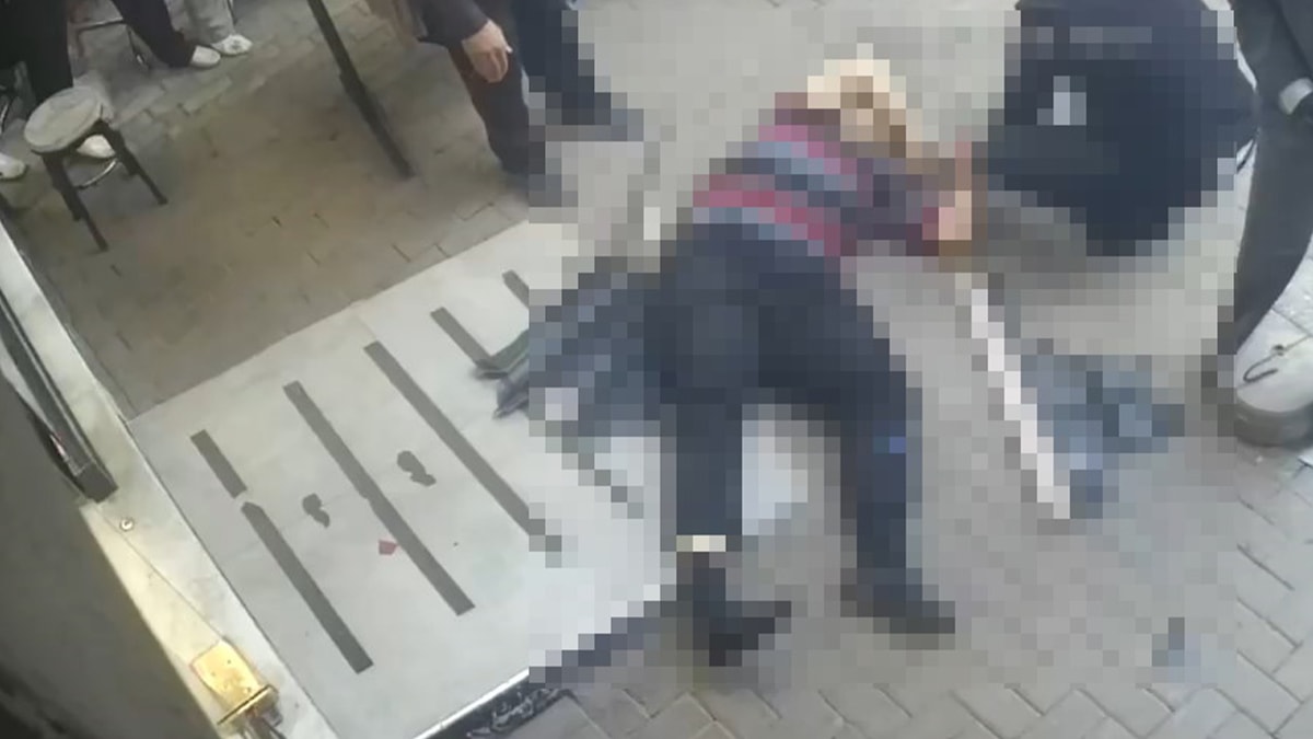 Güvenlik kamerası görüntüsünde, olay sonrası yerde yatan kişi ve çevredeki vatandaşlar bulanıklaştırılmış şekilde görülüyor.