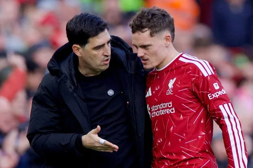 Liverpool teknik ekibinden bir isim, kırmızı forma giyen futbolcuyla saha kenarında konuşuyor.