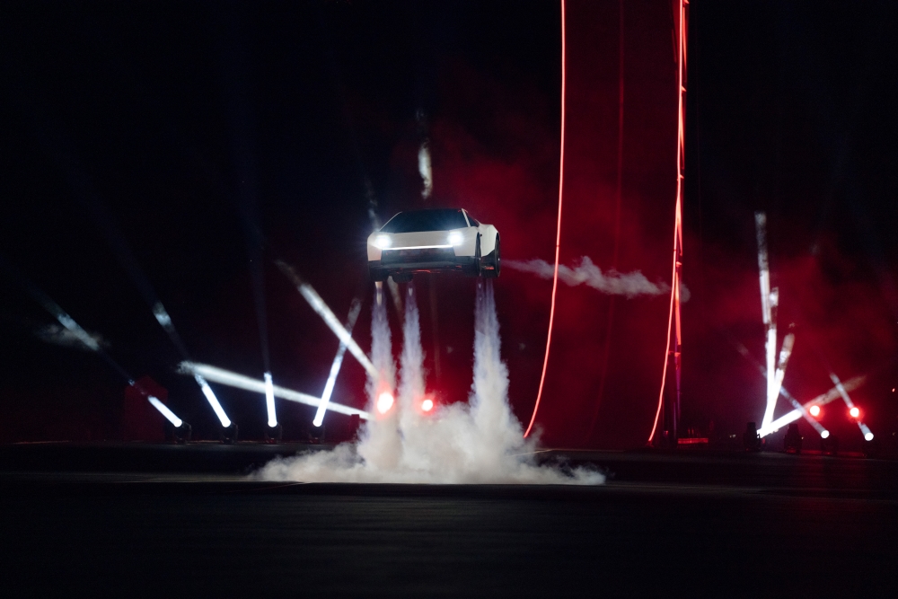 Karanlık pistte ışıklar ve duman eşliğinde havalanmış beyaz Tesla Roadster prototipi.