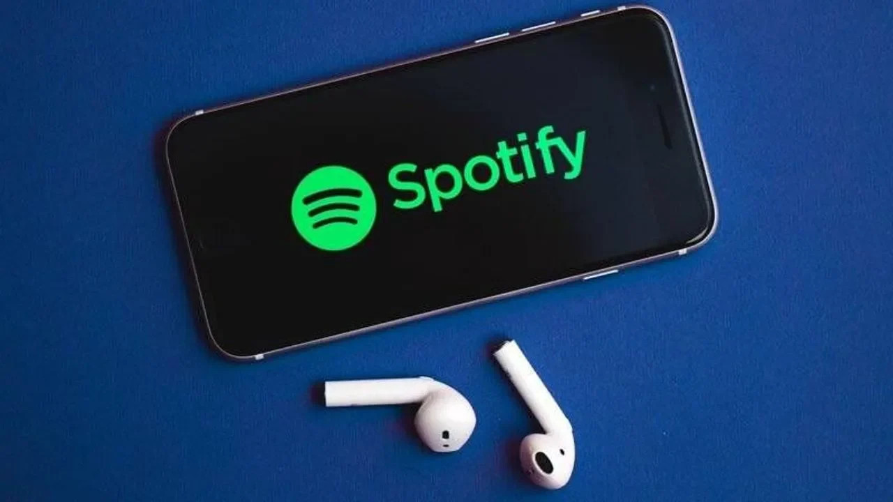 Mavi zemin üzerinde kulaklıkların yanında Spotify yazısı görünen telefon.