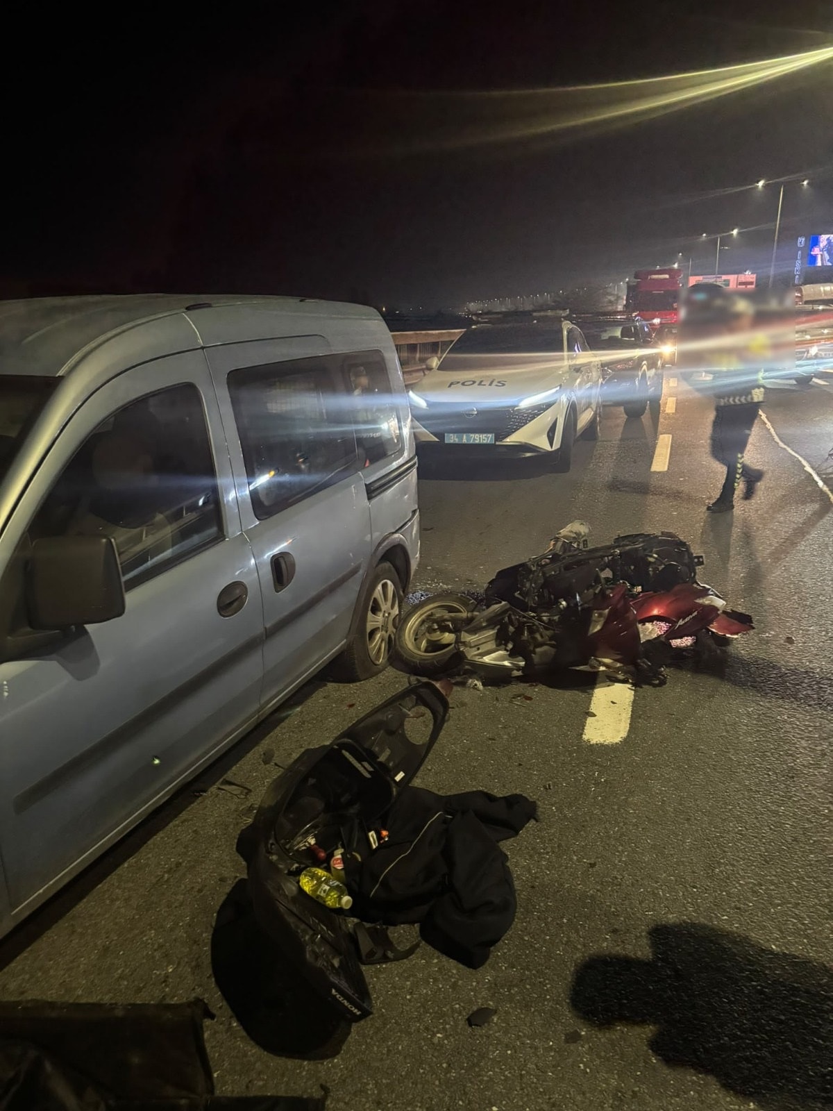 Gece saatlerinde yolda hasar gören motosiklet, hafif ticari araç ve polis ekiplerinin görüldüğü kaza yeri.
