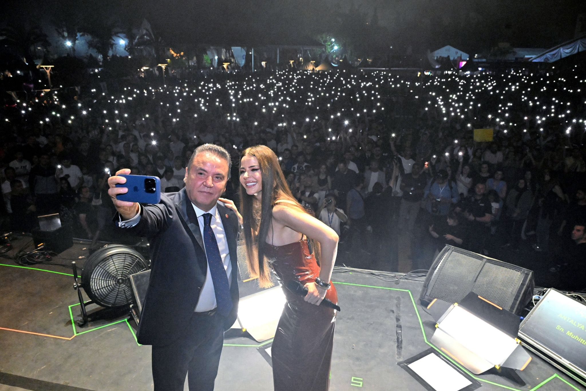 The mayor and an artist are seen on stage at a crowded concert event held at night.